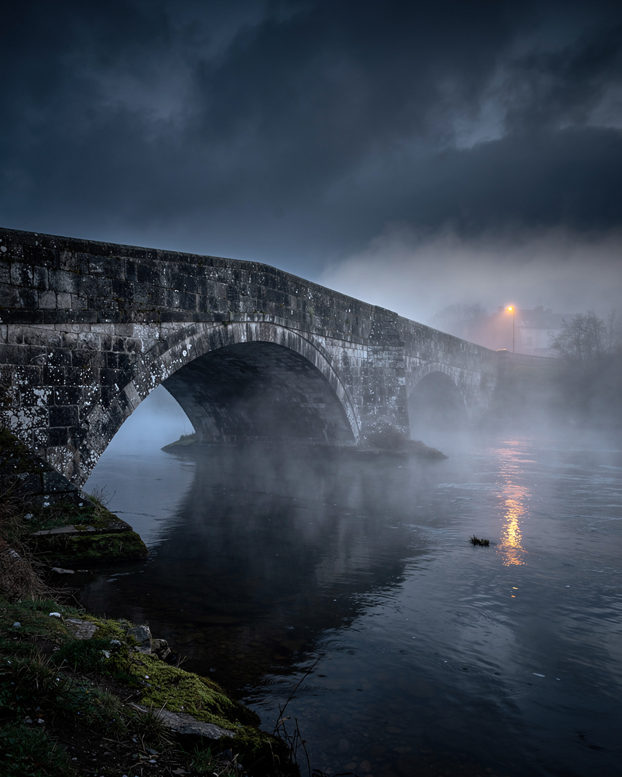 Dark stone bridge over a misty river at dusk